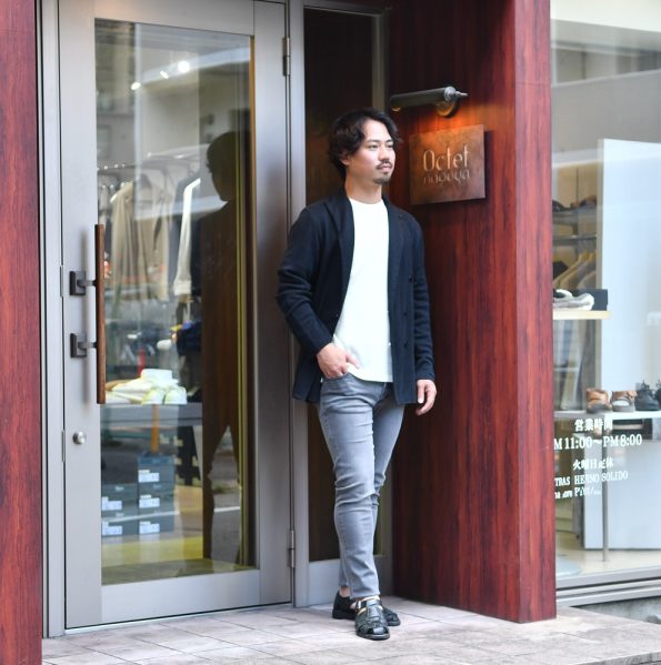 ENTRE AMIS アントレアミ のブラックウォッシュ加工のデニムパンツに、グルカサンダルと、半袖の白Tシャツに黒ジャケットをきれいめカジュアルでコーディネートした写真